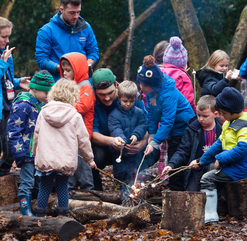 YMCA staff and children toasting marshmellows around a campfire